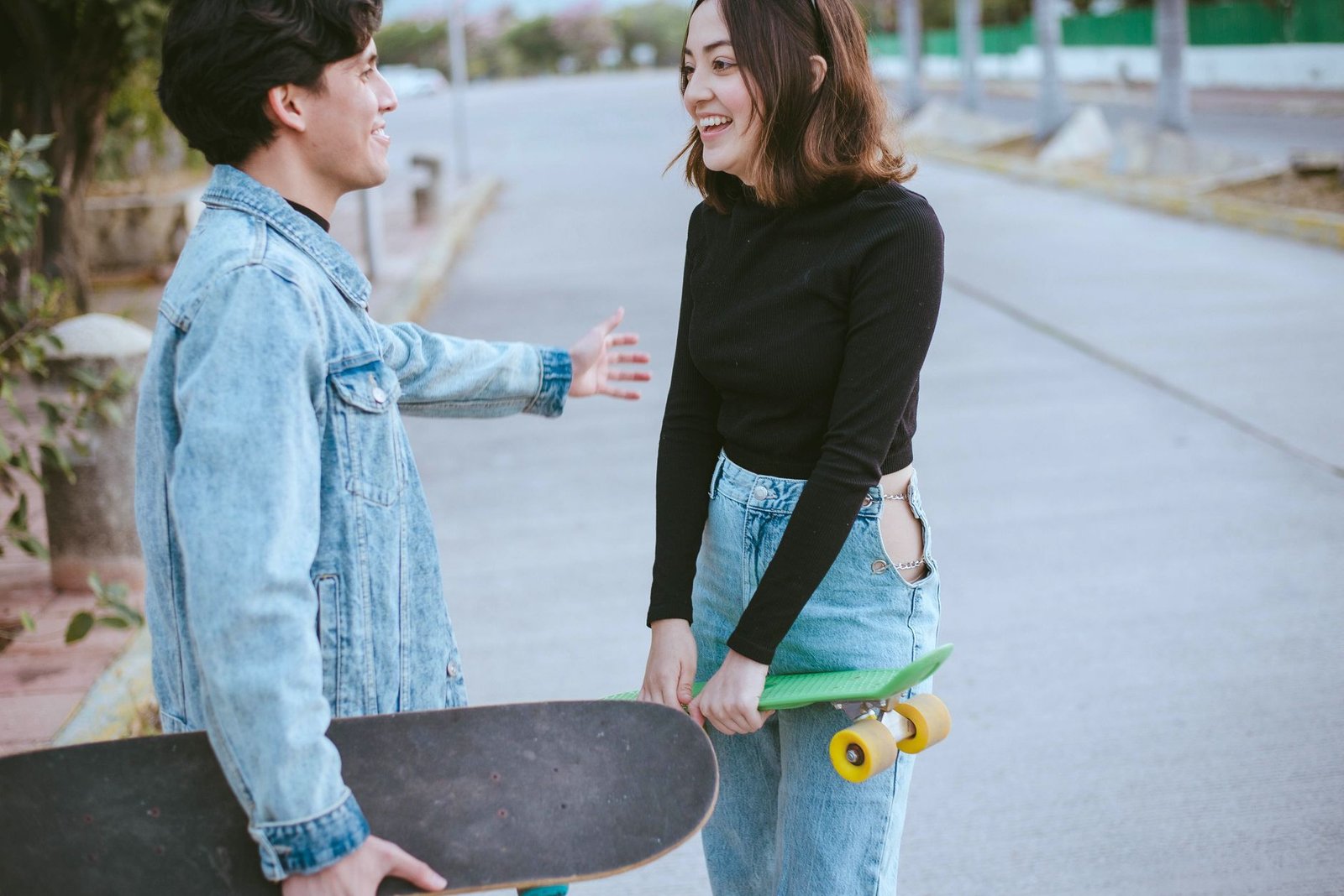 a man in denim jacket looking at the woman in black sweater smiling while holding a skateboard