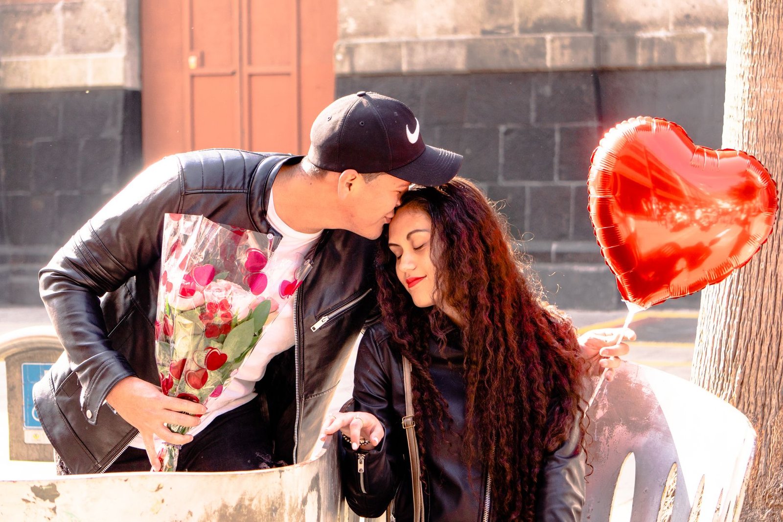 man kissing his girlfriend and holding flowers and a heart shaped balloon