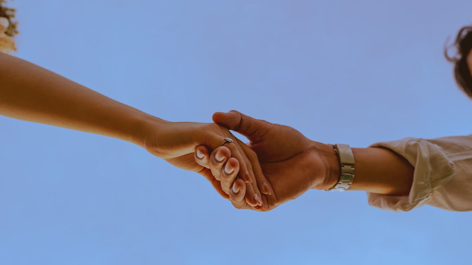 close up of couple holding hands against blue sky